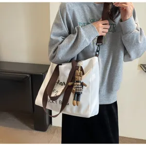 Freizeitorientierte weisse Segeltuchtasche mit braunen Riemen und Anhaenger fuer Studenten.