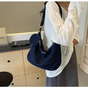 Close-up detail of a dark blue denim crossbody hobo bag with small attached pouch.