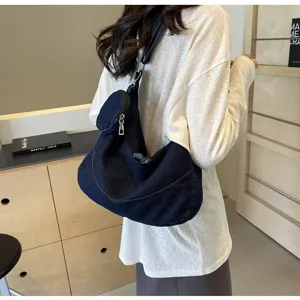 Detail shot of a casual dark blue denim dumpling crossbody bag worn by model, soft style.