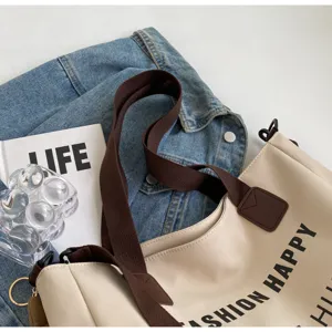 Detailansicht der Canvas-Tragetasche aus beige Stoff mit braunen Riemen und Textdruck.