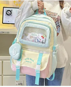 Pastellfarbener Kontrast-Schulrucksack mit transparenter Fronttasche und niedlichen Plüschanhängern.