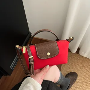 Kleine rote Nylon Umhaengetasche mit braunem Lederklappengriff und goldenen Details