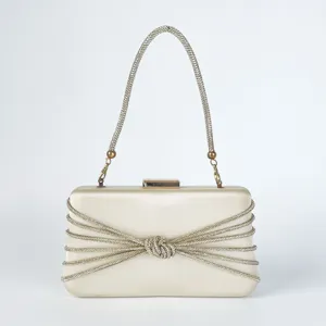 Detailaufnahme einer beige Satin Abendtasche mit funkelnden Strassketten und edlem Knotendesign.