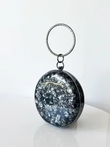 Detaillierte Nahaufnahme der runden Abendtasche mit Muscheltextur und Strass-Ringgriff.