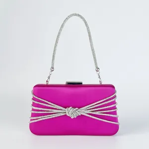 Detailaufnahme der pinken Satin-Abendtasche mit glänzenden Strassketten und Knotendesign.
