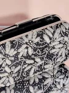 Detailansicht einer eleganten schwarzen Abendtasche mit silberner Perlenstickerei und Metallbügel.
