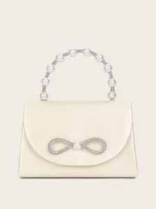 Elegantes Detail von Strassschleife und Perlenhenkel an cremefarbener Satin-Handtasche