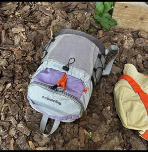 Detailaufnahme des grauen und lila Outdoor-Rucksacks mit Netztasche und orangefarbener Kordel.