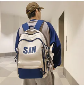 Detail shot of a large-capacity two-tone casual backpack in beige and blue, worn by a male model indoors.