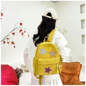 Detailed shot of cute yellow corduroy backpack with star patches worn by model in sweet style