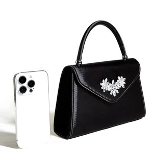 Schwarze Satin-Abendtasche Detailansicht mit funkelnder Kristall-Blumenbrosche und Henkel.