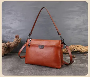 Close-up detail of brown leather shoulder bag featuring multiple zippered layers.