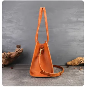 Orange leather handbag side detail showing dual handles and adjustable shoulder strap hardware.
