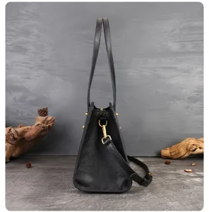 Detailed side view of black leather shoulder bag with metal hardware and sturdy double handles.