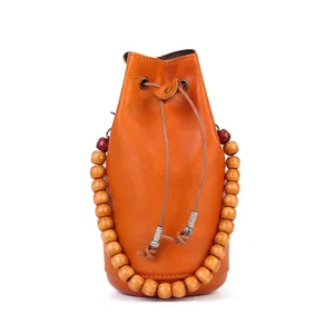 Handmade vegetable-tanned leather bucket bag with wooden bead handle and drawstring closure.