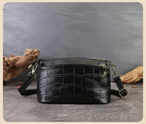 Dettaglio in primo piano di borsa a tracolla in pelle nera con stampa coccodrillo e dettagli oro.