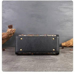 Detailed view of the handbag bottom featuring black leather, floral print trim, and protective metal feet.
