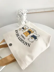 Close-up detail of cute cartoon bear canvas tote bag with snap closure and neutral aesthetic.