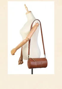 Genuine leather cylindrical shoulder bag with vintage rivet details and adjustable strap design.