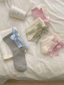 Gros plan détaillé de chaussettes à volants style lolita avec de jolis nœuds sur lit blanc.