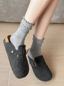 Close-up detail of grey ruffled mid-tube socks paired with stylish felt mule shoes.