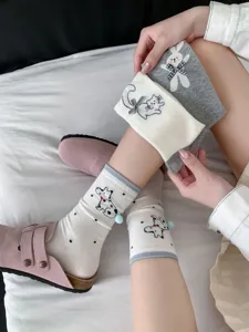 Close-up detail shot of cute cartoon animal socks featuring sweet bows and soft pom-poms.