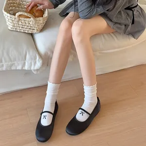 Detail view of white ruffle bow slouch socks with black ballet flats in cozy setting.