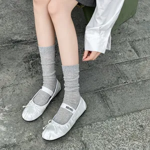 Detail shot of white satin ballet flats paired with gray ribbed slouchy socks for women.