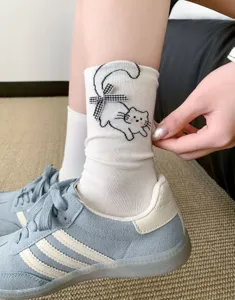 White mid-calf socks featuring a cute cat embroidery and checkered bow detail, styled with sneakers.