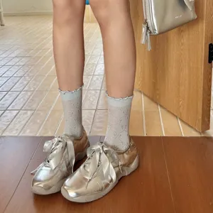 Damen Rüschen transparente Socken Vintage Schleife Muster kombiniert mit silbernen Sneakern.
