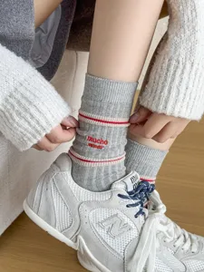 Detail view of grey embroidered mid-tube socks featuring red stripes and cute letter design.