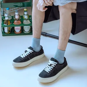 Close-up detail shot of light blue ribbed crew socks worn with black casual sneakers indoors.