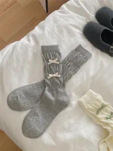 Detailopname van grijze sokken met schattige crèmekleurige strikken, zacht gebreid.