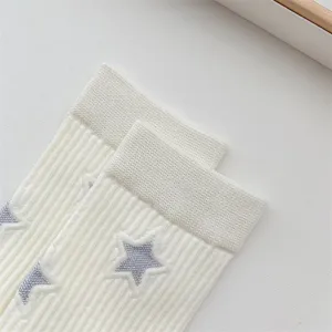 Close-up of white women mid-calf socks with knitted silver star patterns and ribbed cuffs.