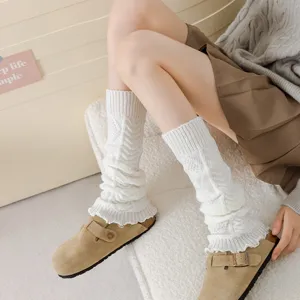 Close-up detail of cozy white cable knit slouch socks worn with suede clogs on fluffy cushion.