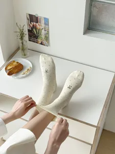 Detailed view of beige slouchy socks featuring delicate black bow embroidery for spring.