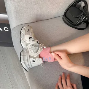 Detail view of pink women short socks with letter print, worn with chunky sneakers on grey sofa.