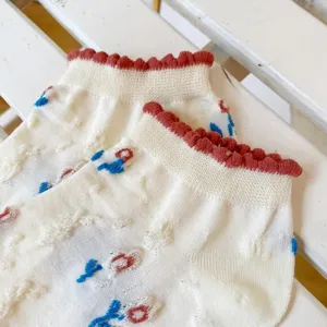 White mesh lace short socks with red ruffled edge and floral embroidery details, detail shot.