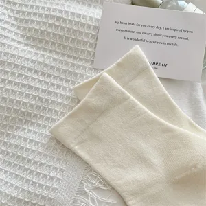 Close-up of white ribbed crew socks styled on textured waffle fabric with a card prop.