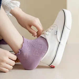 Detail view of cute purple ruffle ankle socks with heart pattern worn with casual white shoes.