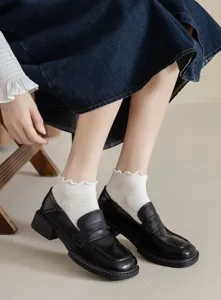 Close-up detail of white ruffle ankle socks with cute heart patterns worn with shoes.