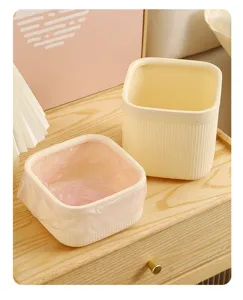 Detailansicht des kleinen cremefarbenen Plastik-Tischmülleimers mit rosa Müllbeutel auf Holztisch.