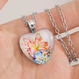 Hart glas hanger ketting met een fijn vlinder en bloem motief detailopname dichtbij.