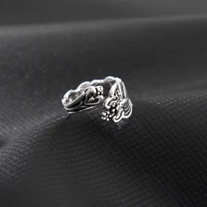 Dettaglio anello aperto in argento vintage, motivo intagliato complesso su sfondo in tessuto mesh.