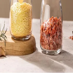 Gros plan pot à épices en verre avec grains jaunes et sel rouge sur plateau en bois.