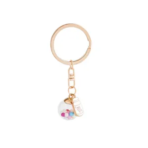 Portachiavi in oro rosa con sfera di vetro e ciondolo a forma di bottiglia di latte.