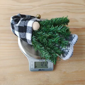 Dettaglio della bambola gnomo di Natale con cappello a quadri nero e bianco, rami di pino e peluche morbido.