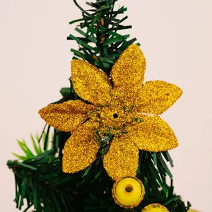 Gros plan détaillé d'une fleur scintillante dorée brillante sur un mini sapin de Noël artificiel.