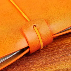 Détail de couverture de carnet en cuir orange, vue de près de sangle élastique agenda