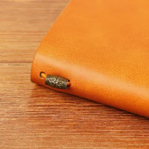 Gros plan d'un carnet de notes en cuir vintage A6 avec bande élastique et breloque en métal.